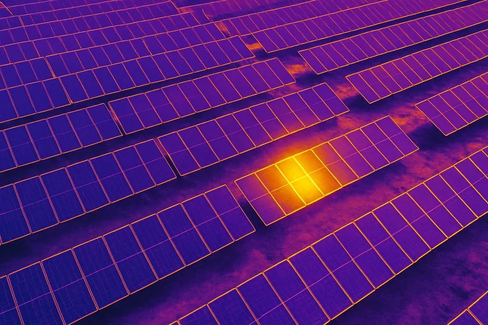 Drone-mounted thermal camera scanning rows of ground-mounted solar panels on an Alberta solar farm, with warmer panels showing as bright hot spots in the infrared view.